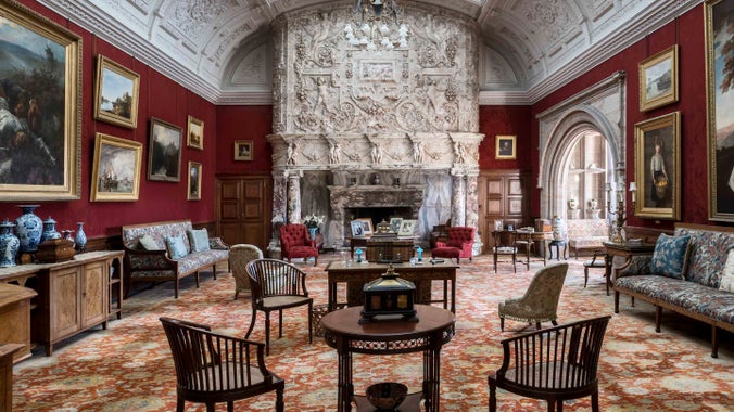 The Drawing Room at Cragside with its intricately carved fireplace surround, curved ceiling and dining room furniture, including tables, chairs and couches